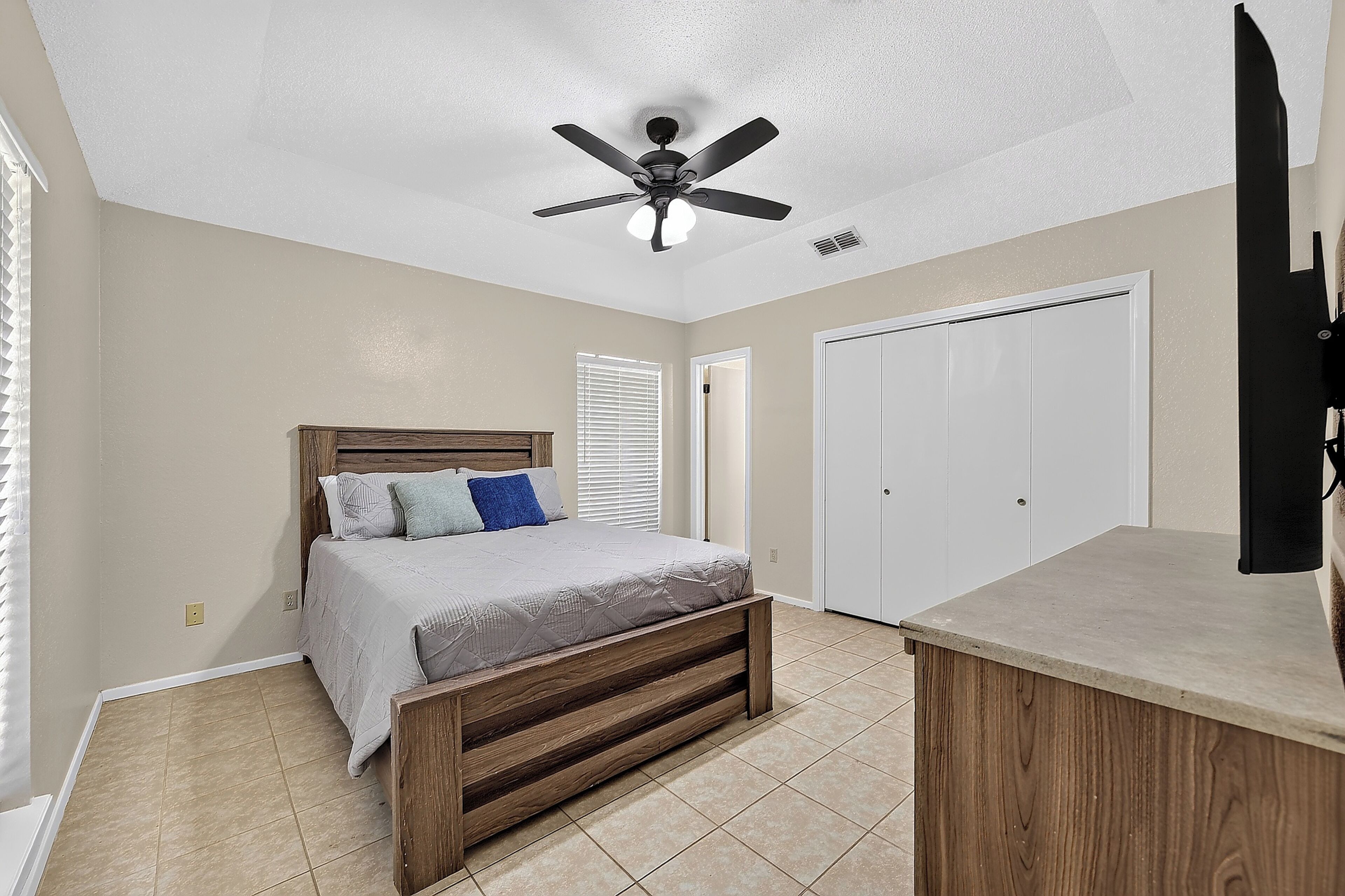 A bedroom with a bed, a ceiling fan, a wardrobe, and a door.