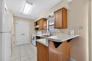 Une cuisine de taille réduite équipée d’un réfrigérateur, d’un four, d’une cuisinière et de meubles de rangement en bois.