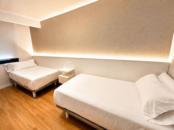 A hotel room with two single beds, a bedside table, and a wall-mounted light fixture. - O LAR DE LUCI (Nigrán)