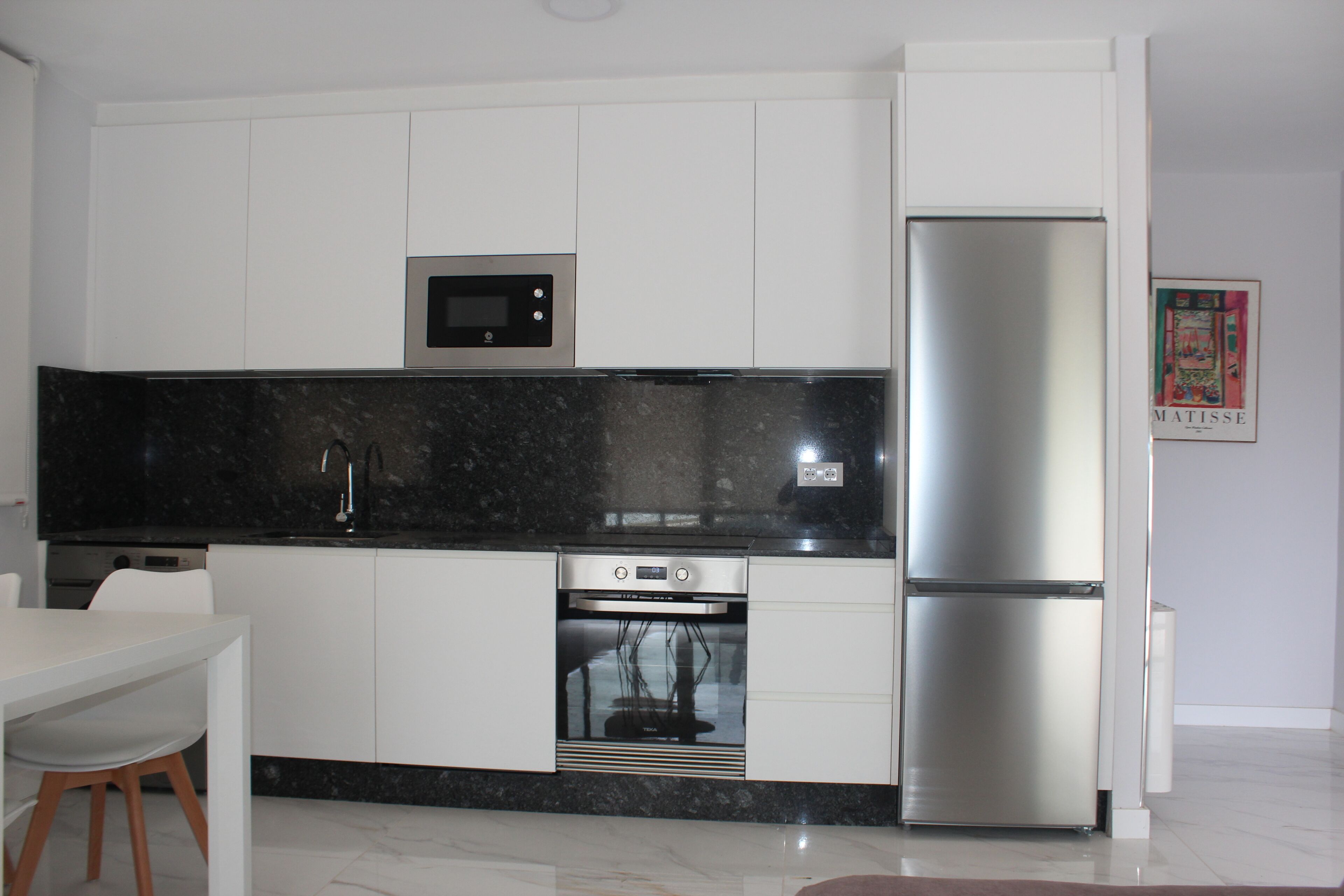 A modern kitchen with white cabinetry, a black countertop, a built-in microwave, a stainless steel refrigerator, and a dishwasher.