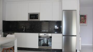 A modern kitchen with white cabinetry, a black countertop, a built-in microwave, a stainless steel refrigerator, and a dishwasher.
