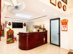 A reception area with a wooden reception desk, a wall-mounted television, a clock, and a door with a red decoration. - Collection O Loc Binh Hotel Near Da Lat Market (Xuan Huong - Da Lat)