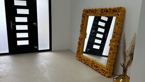 A room with a large mirror with a decorative frame, a door with a keyhole, and a vase with dried plants.