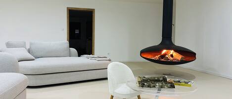 A modern living room with a sofa, a white chair, and a glass table with a fire feature.