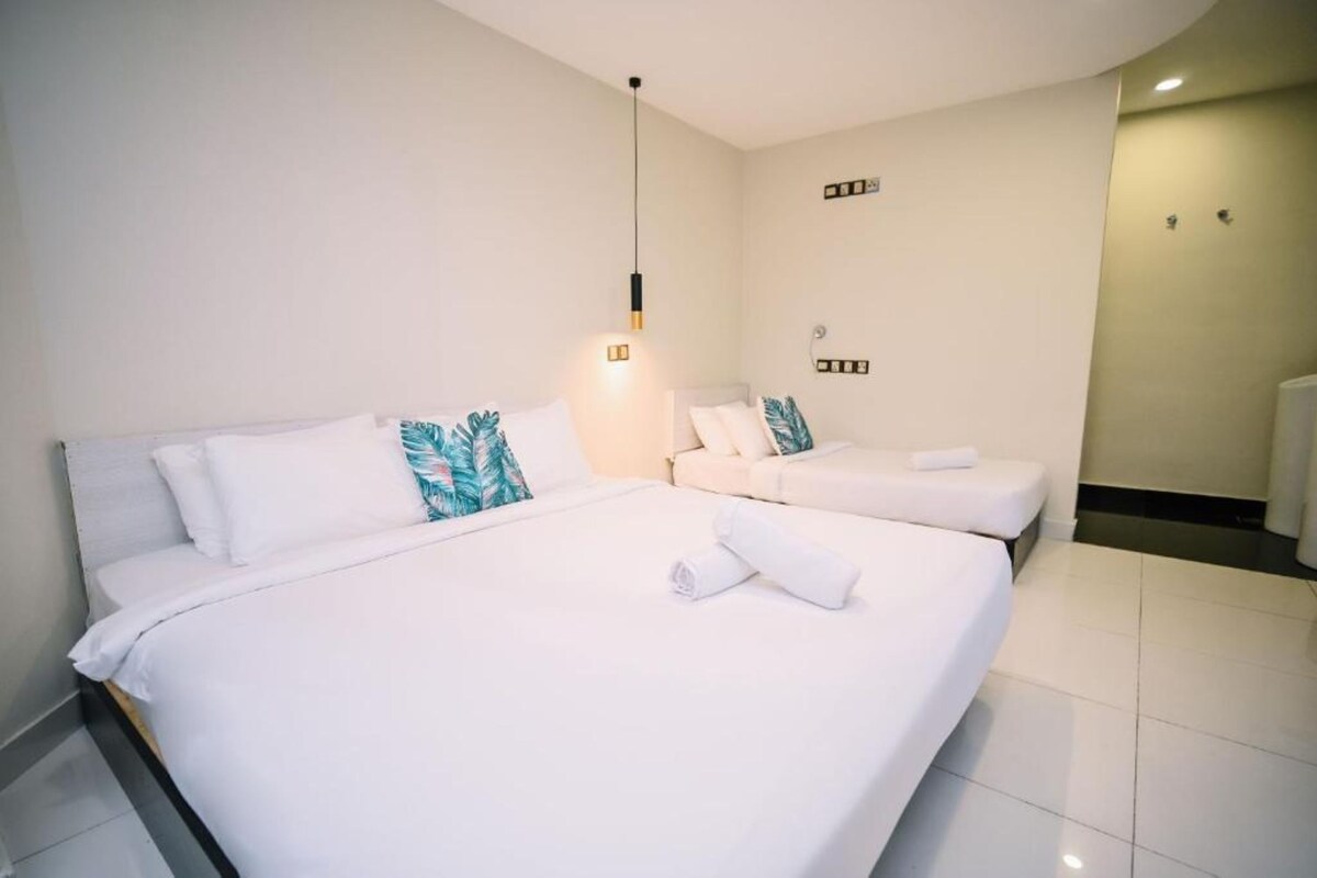 A hotel room with a large bed, a smaller bed, and a bedside table with a lamp.