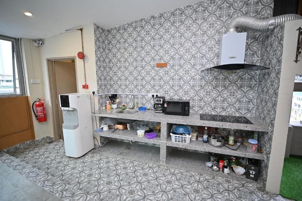 Una cocina compacta con microondas, cafetera y dispensador de agua. Hay un extintor de incendios fijado a la pared, y un salpicadero decorativo.
