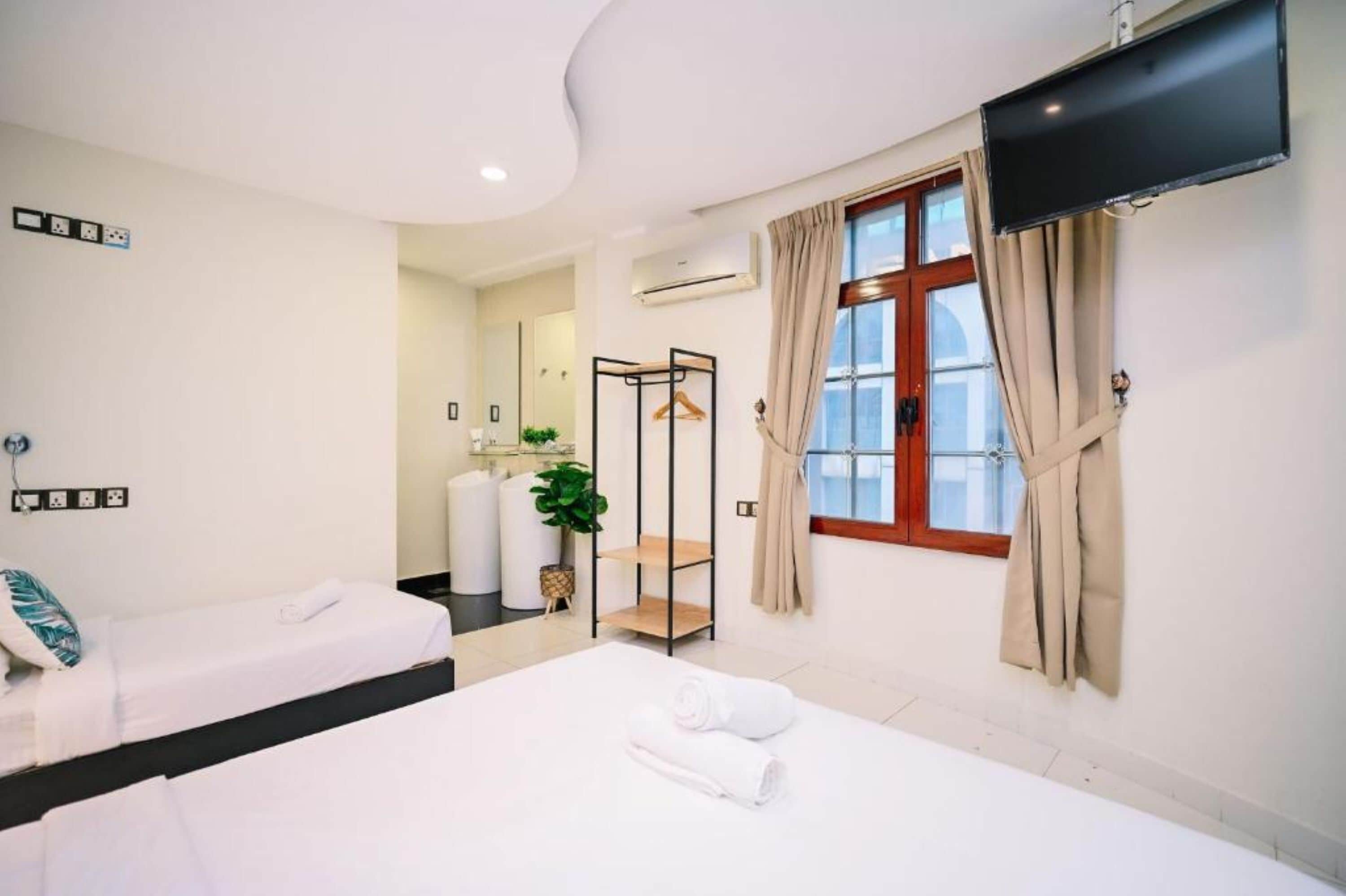 Una habitación de hotel con dos camas, un televisor, una ventana con cortinas y un baño a la vista al fondo.