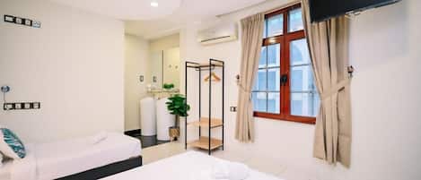 Una habitación de hotel con dos camas, un televisor, una ventana con cortinas y un baño a la vista al fondo.