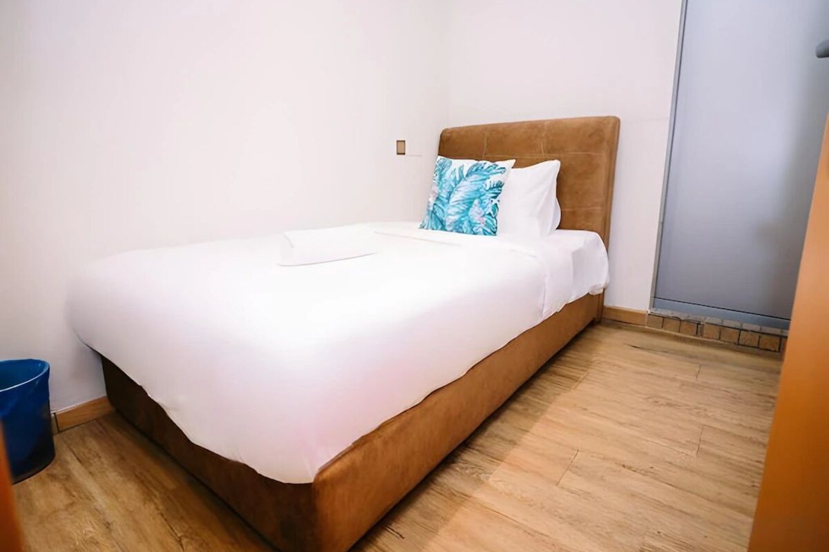 A single bed with a wooden headboard, white bedding, and a blue pillow with a leaf pattern.