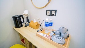 Habitación de hotel con escritorio de madera, cafetera, lámpara, caja de pañuelos, agua embotellada, control remoto, bandeja con un plato y un par de tijeras.