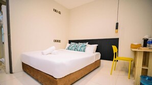 Una cama bien hecha con sábanas blancas, un cabecero de madera y una sola silla amarilla.