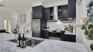 A modern kitchen with dark cabinets, a stainless steel refrigerator, and a marble countertop. - Coastal Clover - 7 James Drive (Carrickalinga)
