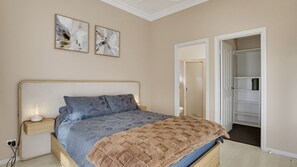 Ein Schlafzimmer mit Bett, Nachttische, einem Kleiderschrank und einer Tür zu einem anderen Raum.