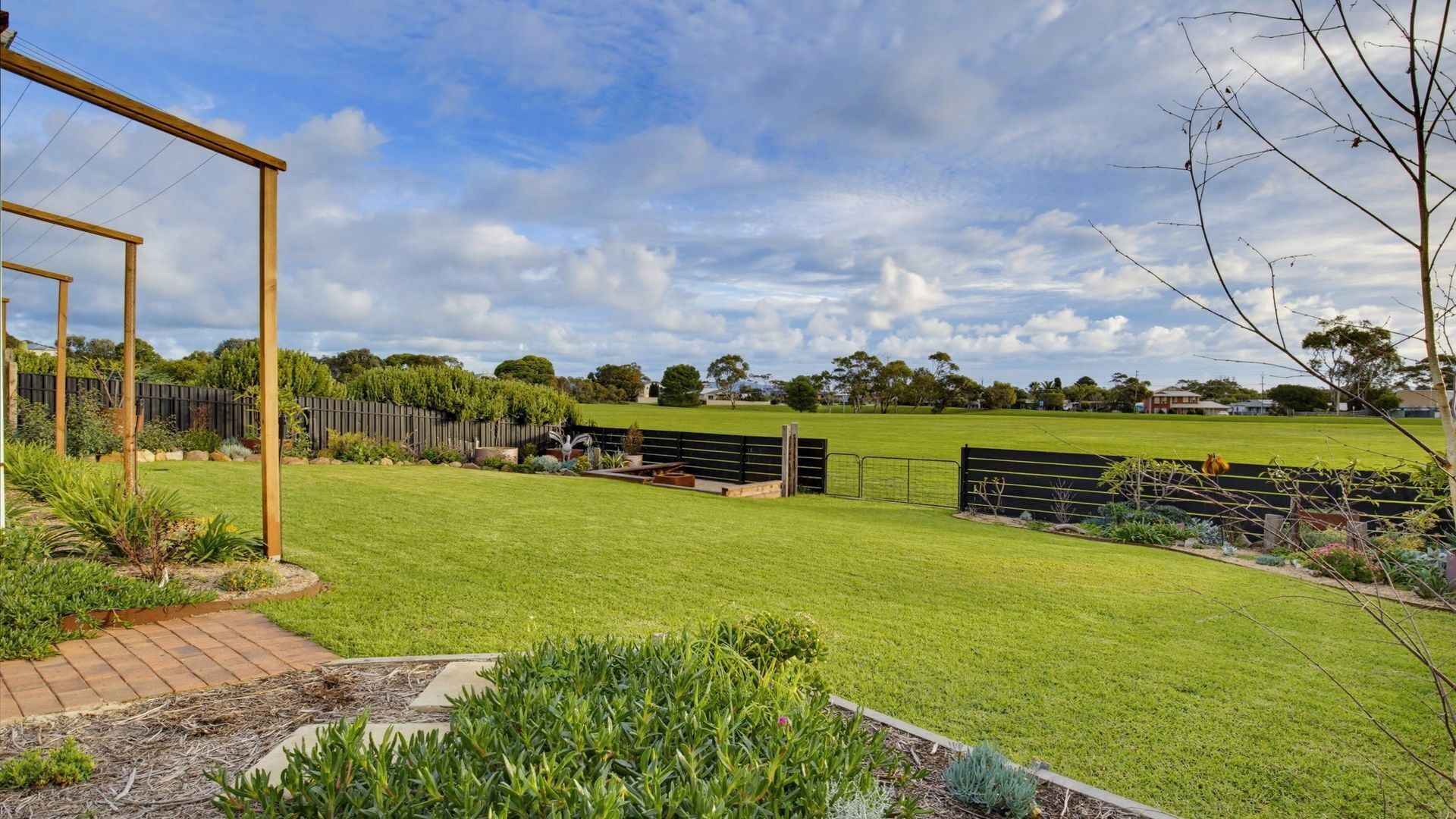 A well-maintained backyard with a wooden pergola, a fenced area, and a variety of plants.