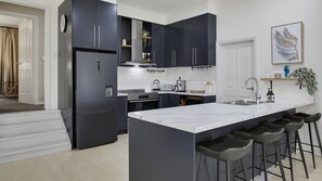 A modern kitchen with dark cabinets, a marble island, and bar stools. - Coastal Clover - 7 James Drive (Carrickalinga)