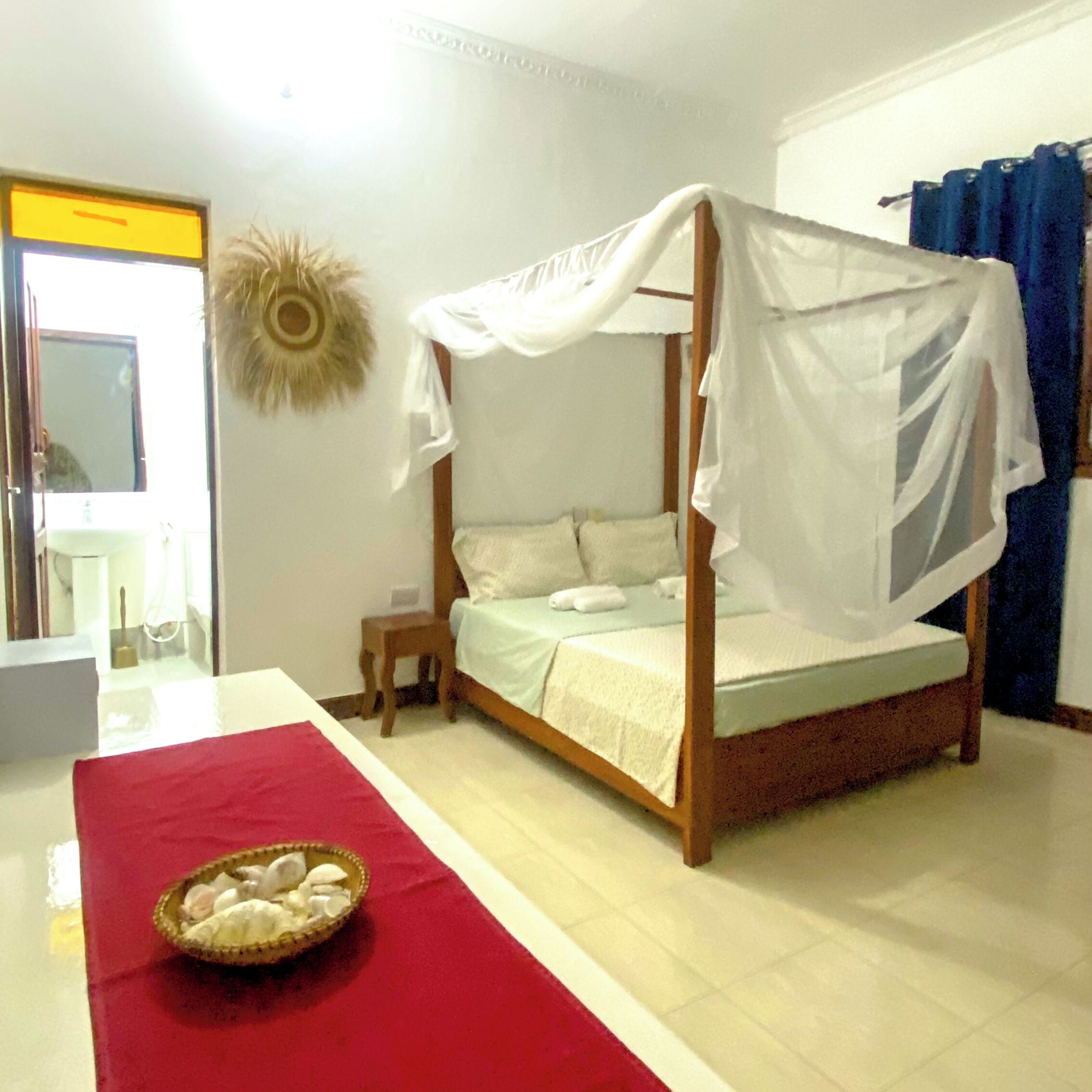 A single bed with a canopy, a small bedside table, and a red runner.