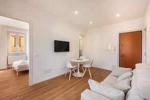 Ein modernes Wohnzimmer mit einer Couch, einem Esstisch mit Stühlen, einem an der Wand befestigten Flachbildfernseher und Holzboden.