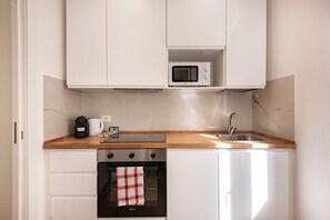 Eine kompakte Küche mit weißen Schränken, einer Mikrowelle, einer Kaffeemaschine und einem Spülbecken.
