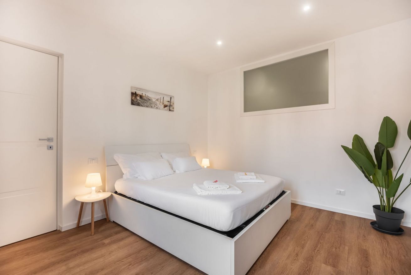 Une chambre à coucher avec un lit, une table de chevet, une lampe et une plante en pot.