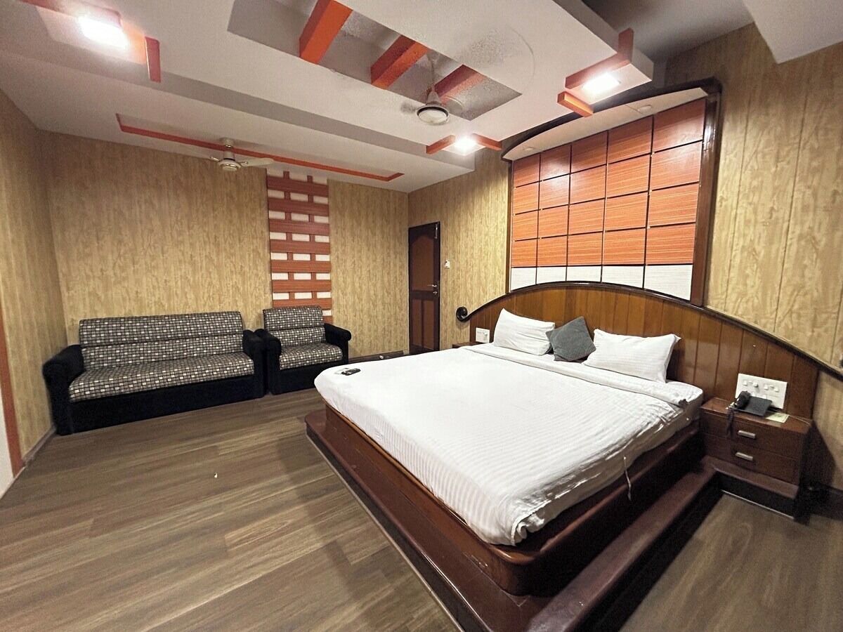 A hotel room with a large bed, a sofa, a nightstand, and a window with blinds.