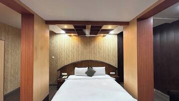 Quarto de hotel com uma cama grande, cabeceira de madeira e um ventilador de teto.
