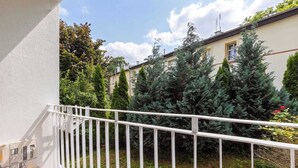 A balcony with a white railing, overlooking a garden with various trees and shrubs. - Cosy Apartment for 6 People | Balcony | Opera Leśna (Sopot)