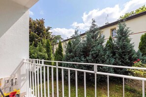 Ein Balkon mit weißer Brüstung, der auf einen Garten mit verschiedenen Bäumen und Sträuchern blickt.