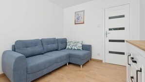 A room with a light blue sofa, a wooden floor, a white door with black handles, and a framed picture on the wall. - Cosy Apartment for 6 People | Balcony | Opera Leśna (Sopot)