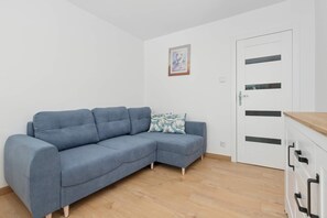 Ein Zimmer mit einem hellblauen Sofa, Holzboden, einer weißen Tür mit schwarzen Griffen und einem gerahmten Bild an der Wand.
