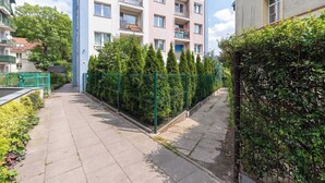 A residential building with multiple balconies, a gated area with greenery, and a clear sky. - Cosy Apartment for 6 People | Balcony | Opera Leśna (Sopot)