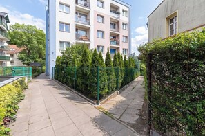 Ein Wohngebäude mit mehreren Balkonen, einem begrünten, umzäunten Bereich und blauem Himmel.