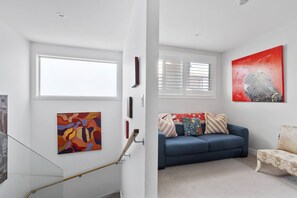 A modern living room with a blue sofa, a coffee table, and a large abstract painting. - 2BR Bondi Retreat with Parking & Walk to the Beach (Bondi Road)
