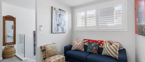 Una sala de estar con un sofá azul, una silla, un cuadro y una ventana con persianas.