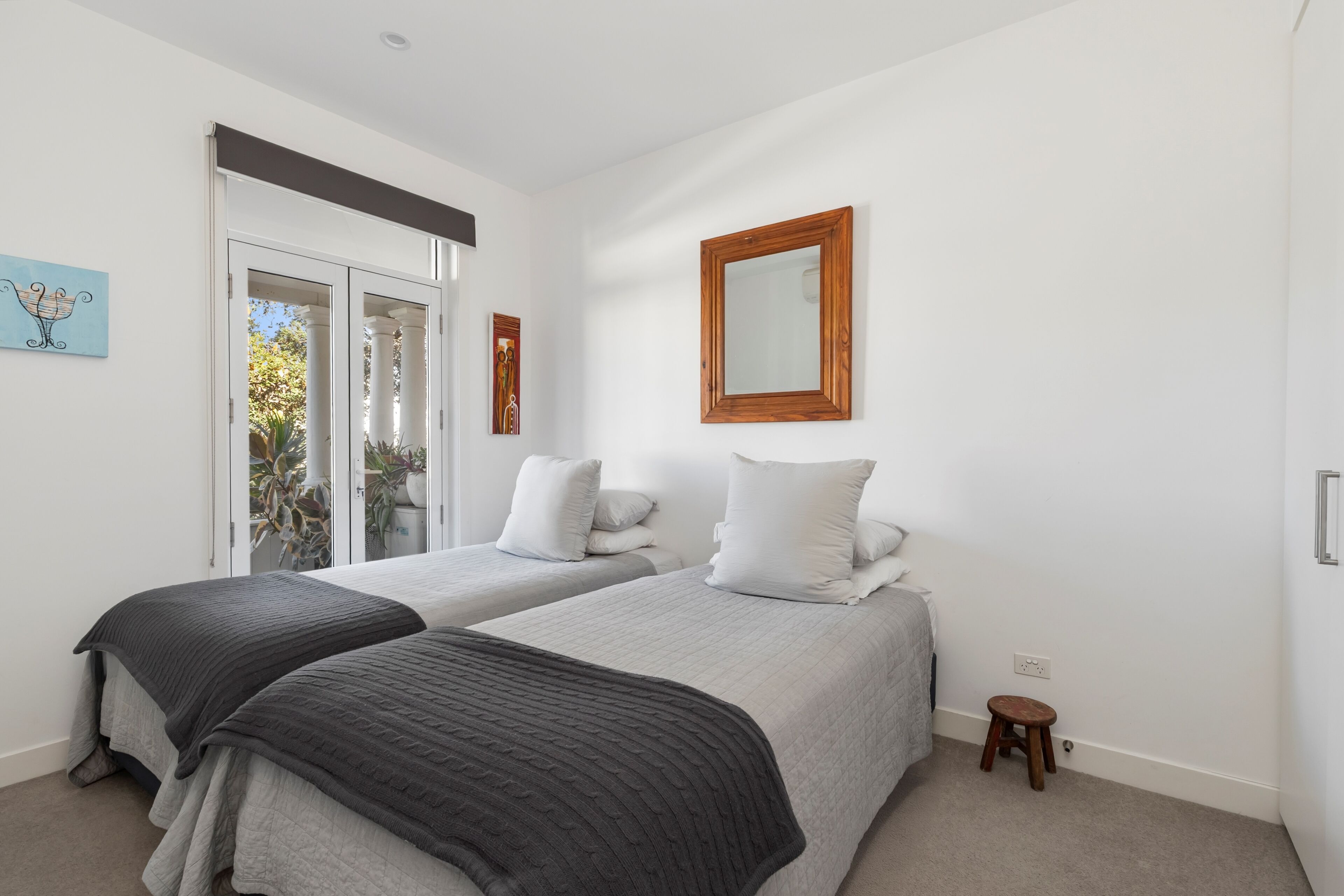 A bedroom with two beds, a wooden-framed mirror, and a small stool.