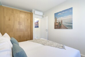 Ein Schlafzimmer mit einem Holzschrank, einem Bett mit weißer Bettwäsche, einem Bild von einem Steg und einer Klimaanlage.