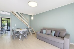 Ein modernes Wohnzimmer mit Treppe, einem Essbereich mit Stühlen und einer Couch mit Kissen.