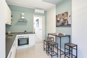 A modern kitchen with a built-in oven, a gas stove, and a stainless steel sink. There are two stools and a small table with a cup and a plate of food. - Regarda - Basiliko View Apartment with lake view and pool (Lazise)