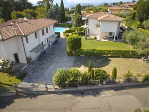 A residential area with a swimming pool, paved courtyard, and surrounding greenery. - Regarda - Basiliko View Apartment with lake view and pool (Lazise)