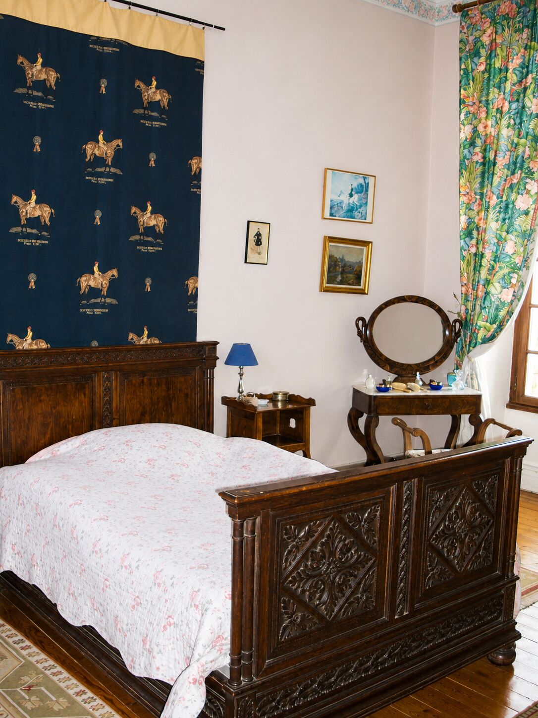 Een slaapkamer met een houten bed, nachtkastje, spiegel en wandtapijt.