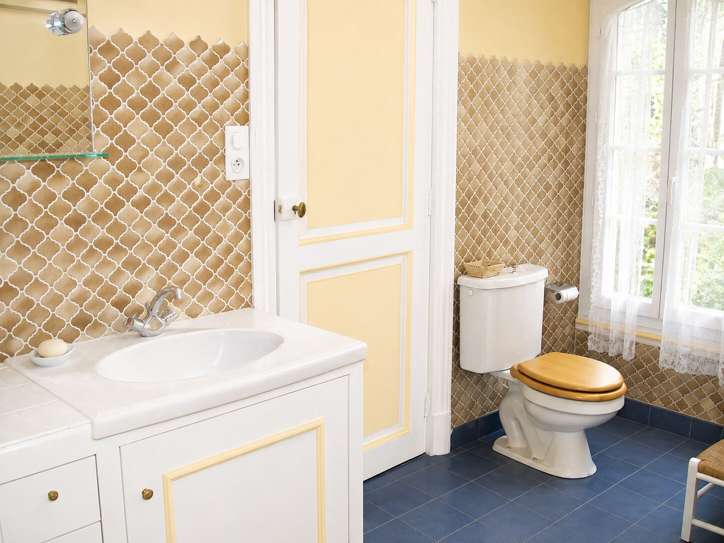 Un baño con lavamanos blanco, inodoro con asiento de madera y ventana con vista a follaje.