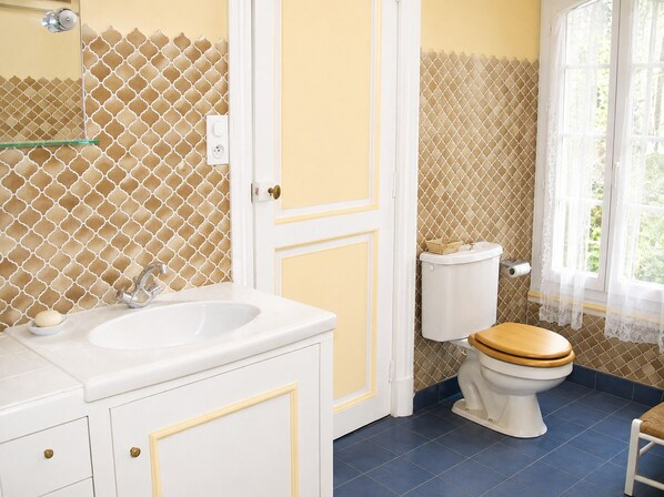 A bathroom with a white sink, a toilet with a wooden seat, and a window with a view of greenery.