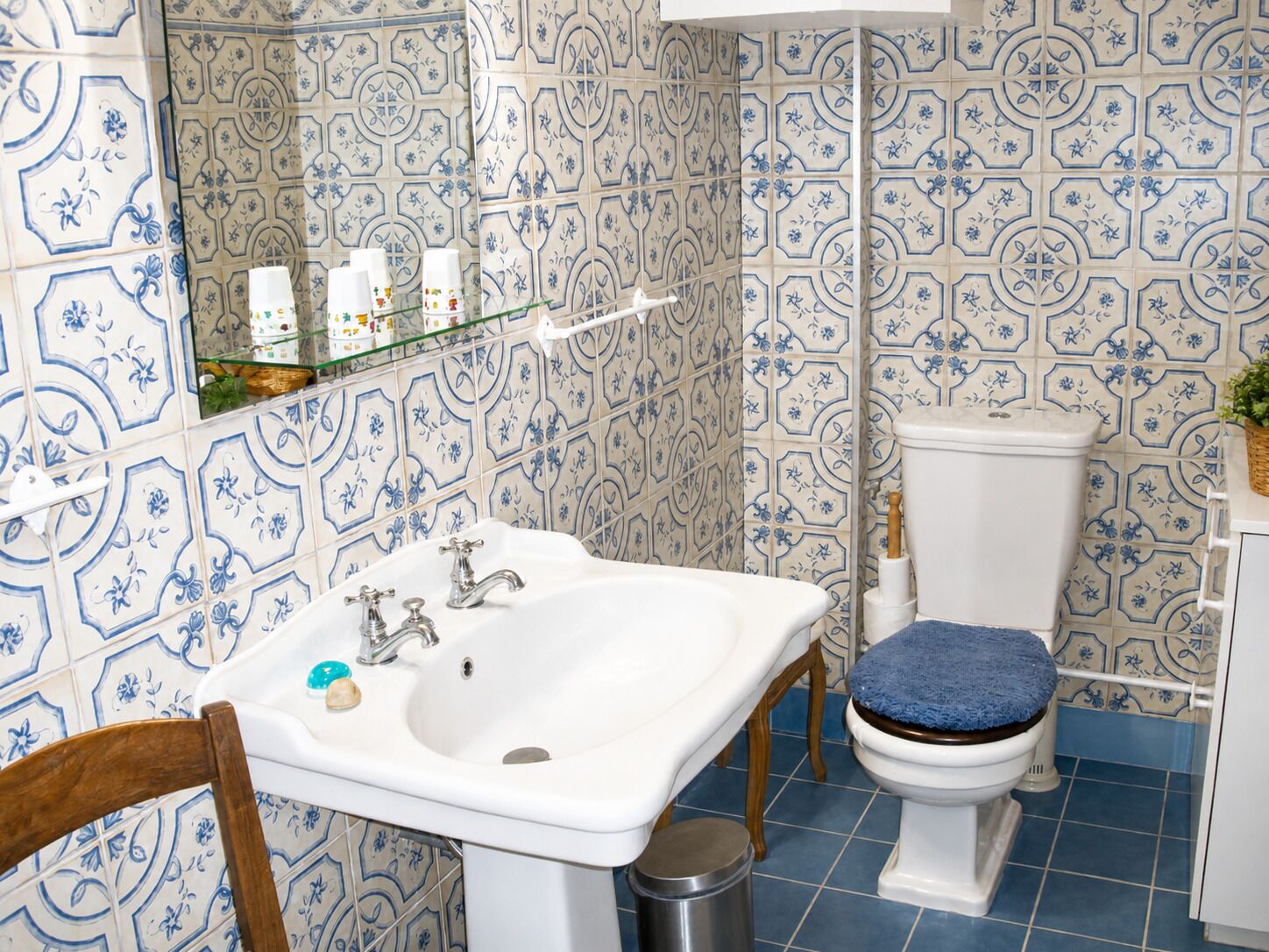 A bathroom with a white sink, a toilet with a blue seat, and blue patterned tiles on the walls and floor.