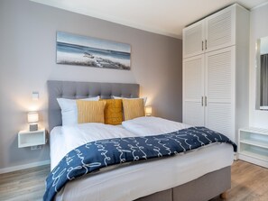 A bedroom with a bed, bedside lamps, a painting, and a wardrobe. - Familienwohnung in der Nahe der Ostsee (Lübeck)