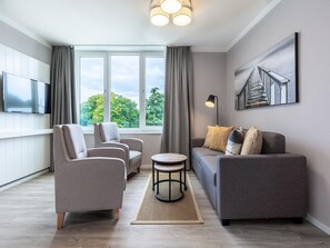 A modern living room with a sofa, two armchairs, a coffee table, and a TV mounted on the wall. - Familienwohnung in der Nahe der Ostsee (Lübeck)