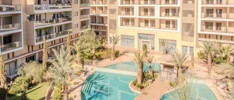 A multi-story hotel with a central swimming pool surrounded by palm trees and outdoor seating.