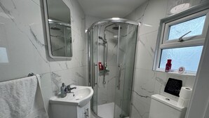 Un baño con ducha envuelta en vidrio, lavabo, inodoro y ventana con vistas.