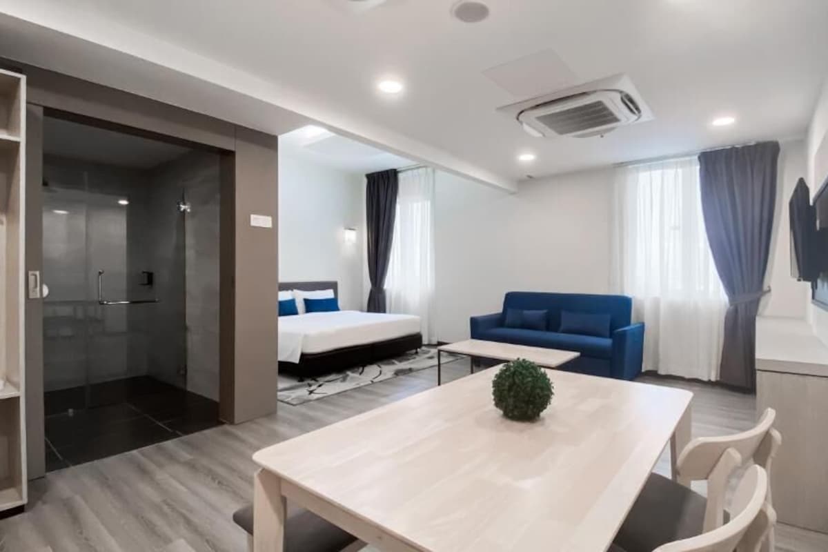 Une chambre d’hôtel moderne avec un lit, un canapé bleu, une table à manger et un espace douche.