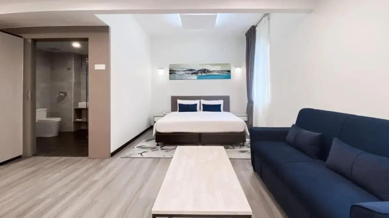 Una habitación de hotel moderna con cama, sofá, una mesita y zona de ducha.