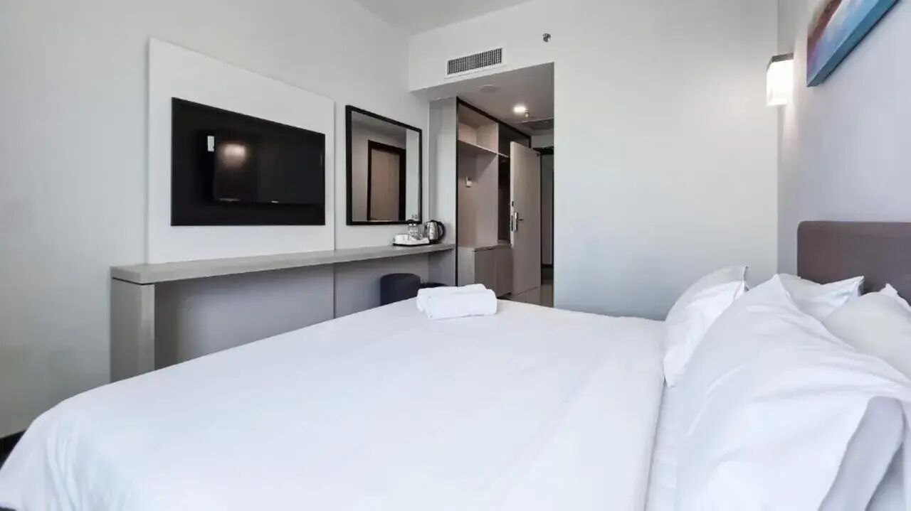 Habitación de hotel con cama, televisor de pantalla plana en la pared, espejo y armario.