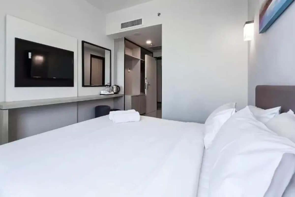A hotel room with a bed, a flat-screen TV mounted on the wall, a mirror, and a wardrobe.